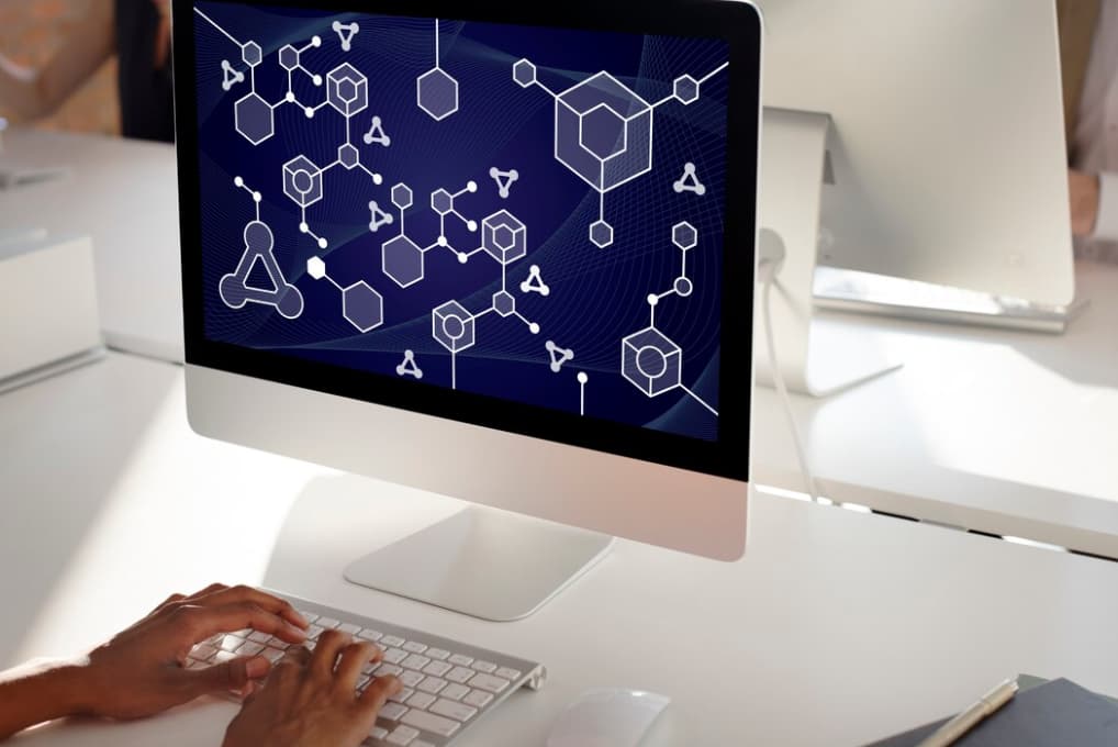 A person works on a computer with a hexagonal, network-themed background